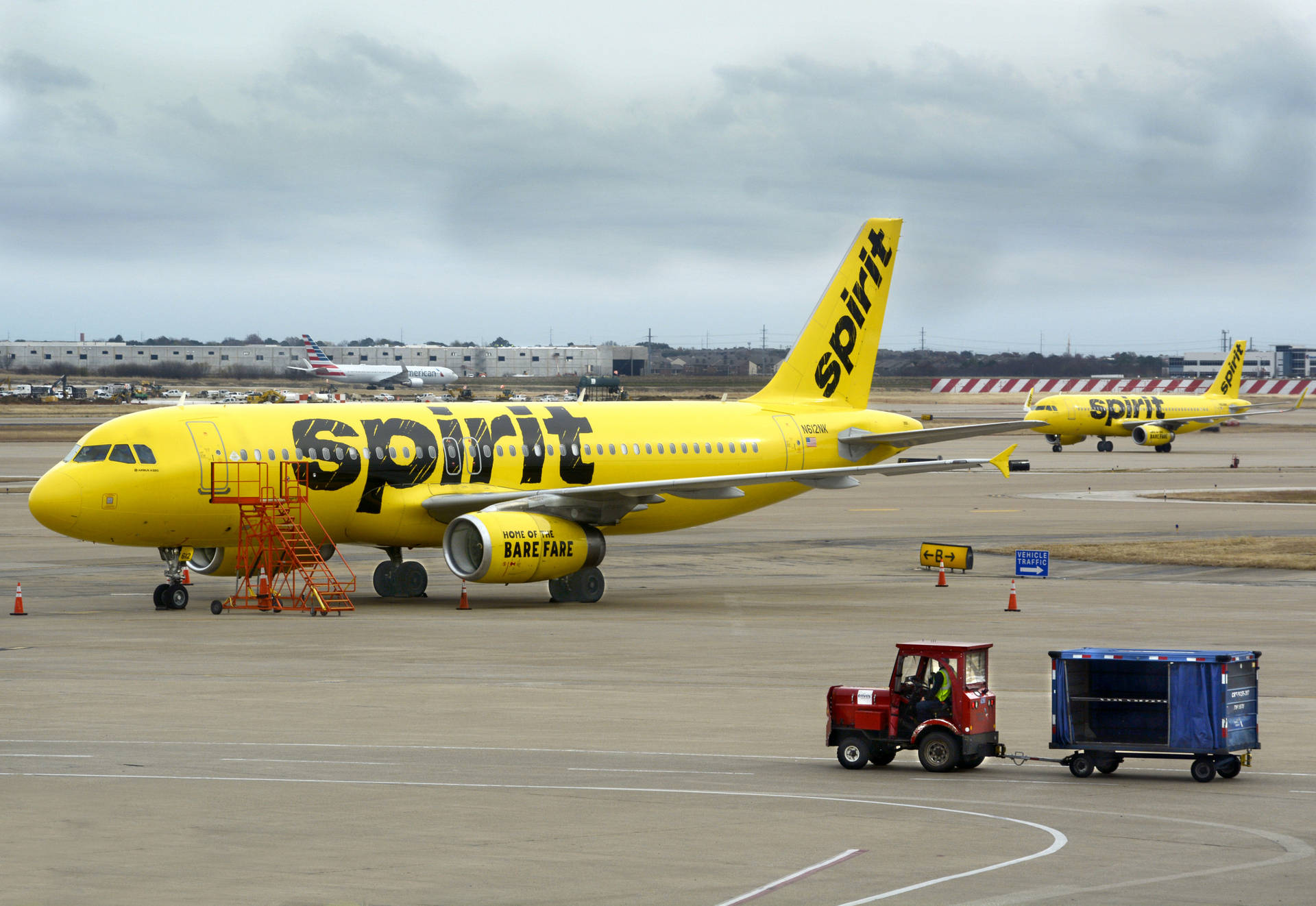 黃色Spirit Airlines飛機停在機場停機坪，附近有地勤服務車輛。