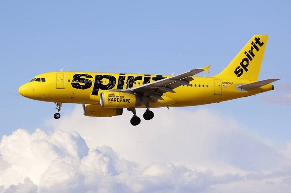 黃色Spirit Airlines飛機放下起落架在白雲上飛行。