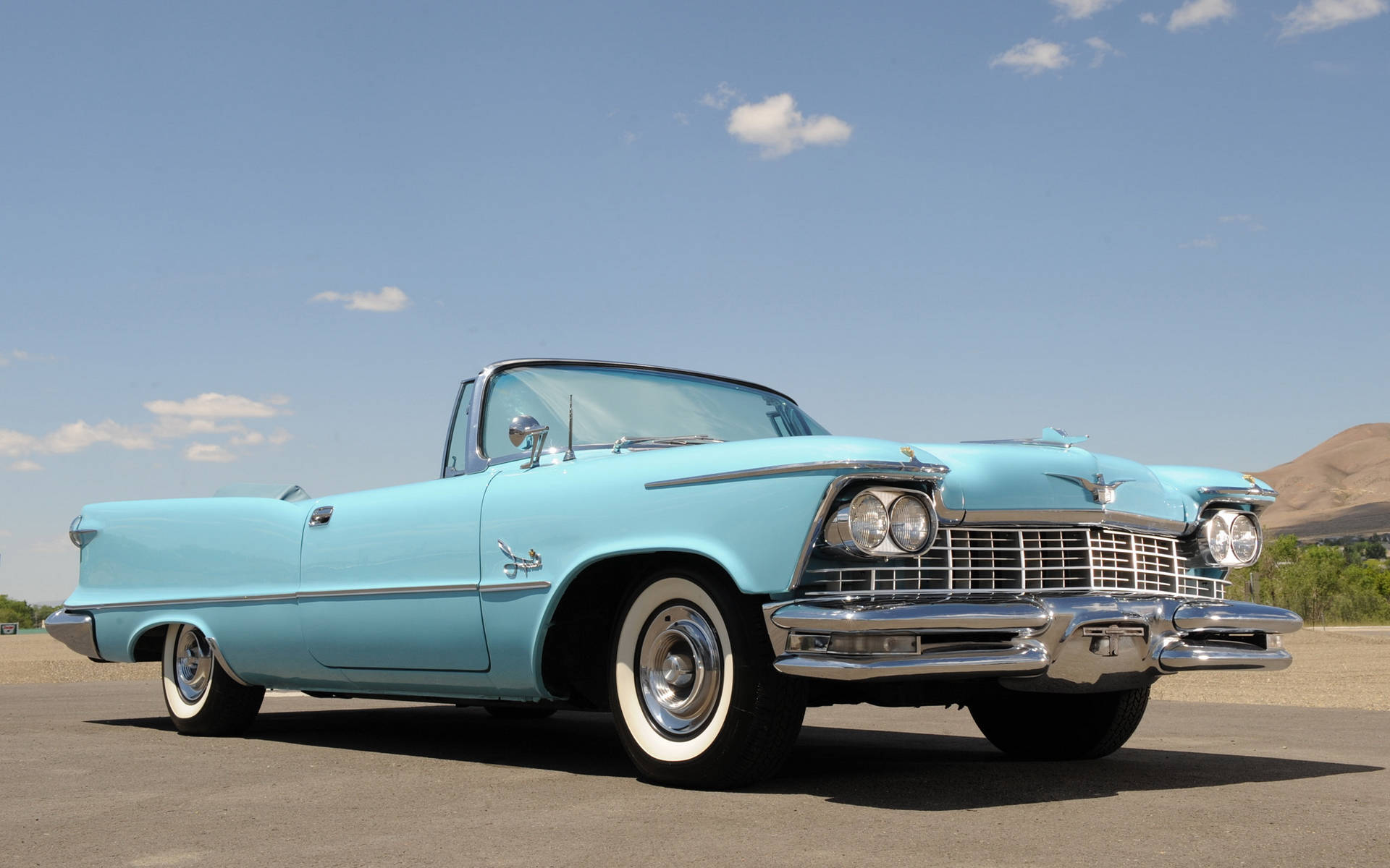 精緻 1958 Chrysler Imperial Convertible 壁紙 — 一輛復古淺藍色敞篷車，帶有鍍鉻細節，停在鋪砌的道路上，天空清澈湛藍，有零星雲朵。