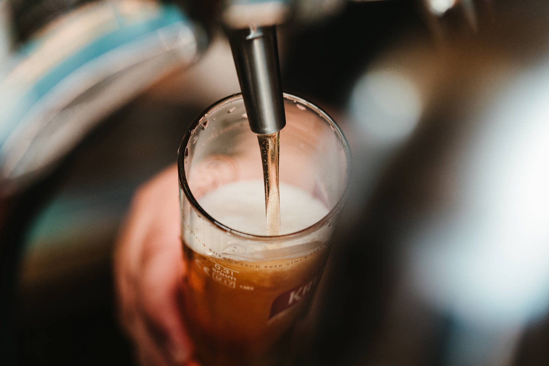 手持玻璃杯，琥珀色啤酒從水龍頭倒出，帶有泡沫頭