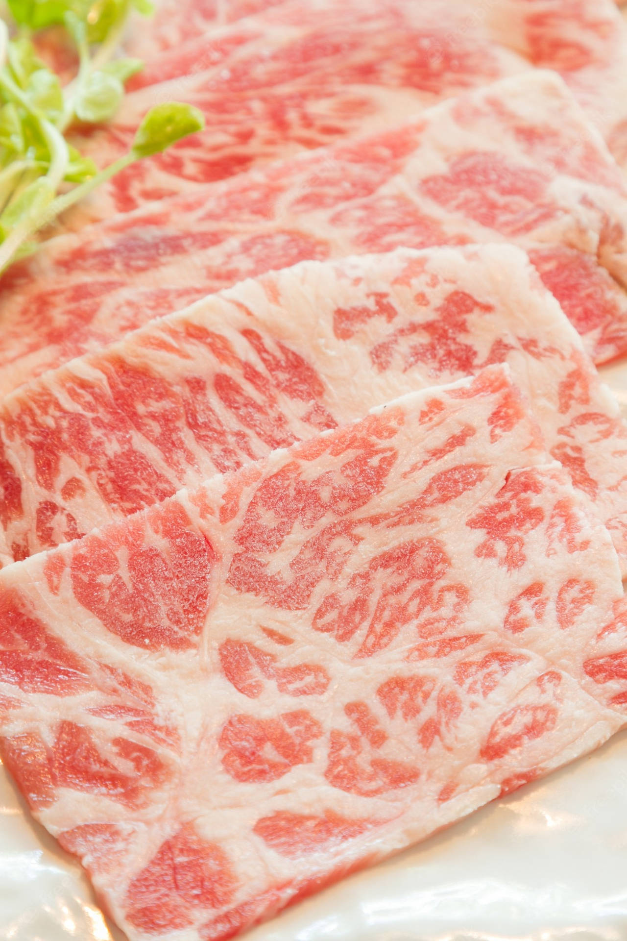 白碟上嘅薄切大理石紋牛肉片配新鮮蔬菜。