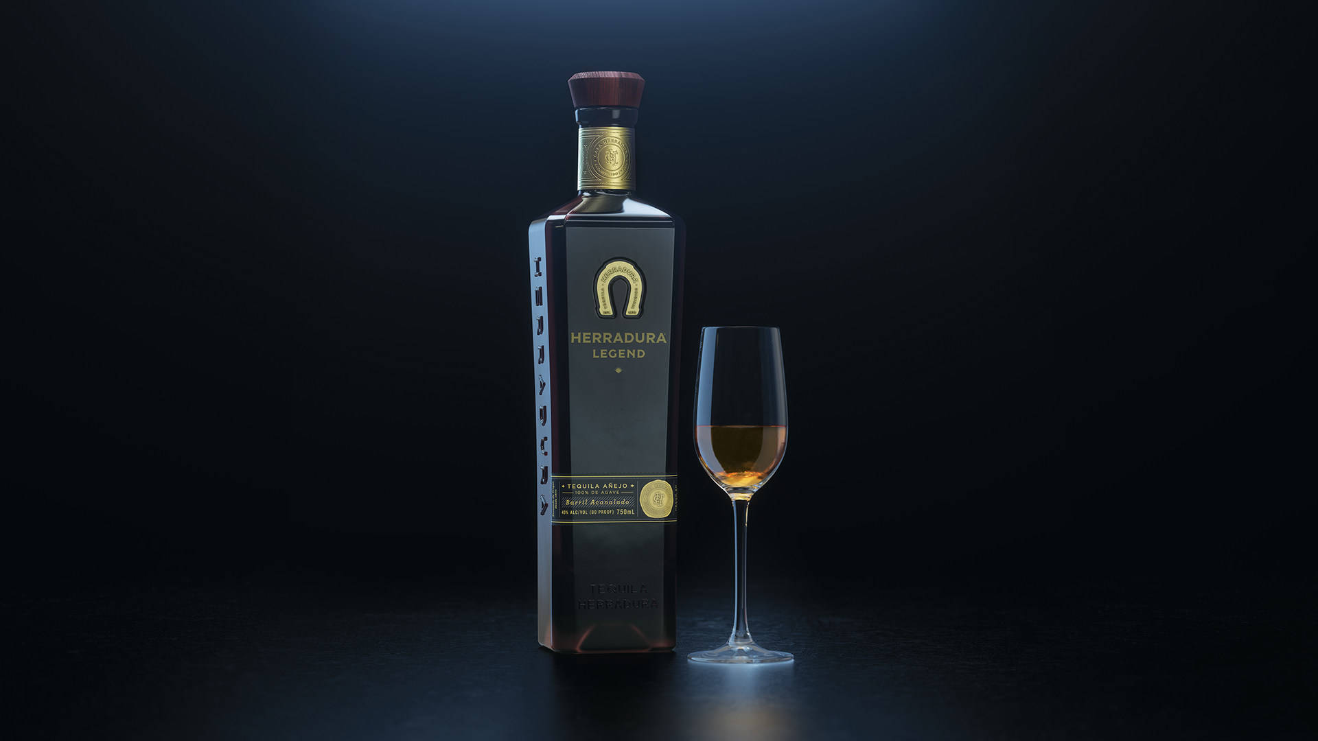 在聚光燈下，深色表面上的Herradura Legend龍舌蘭酒瓶和玻璃杯。
