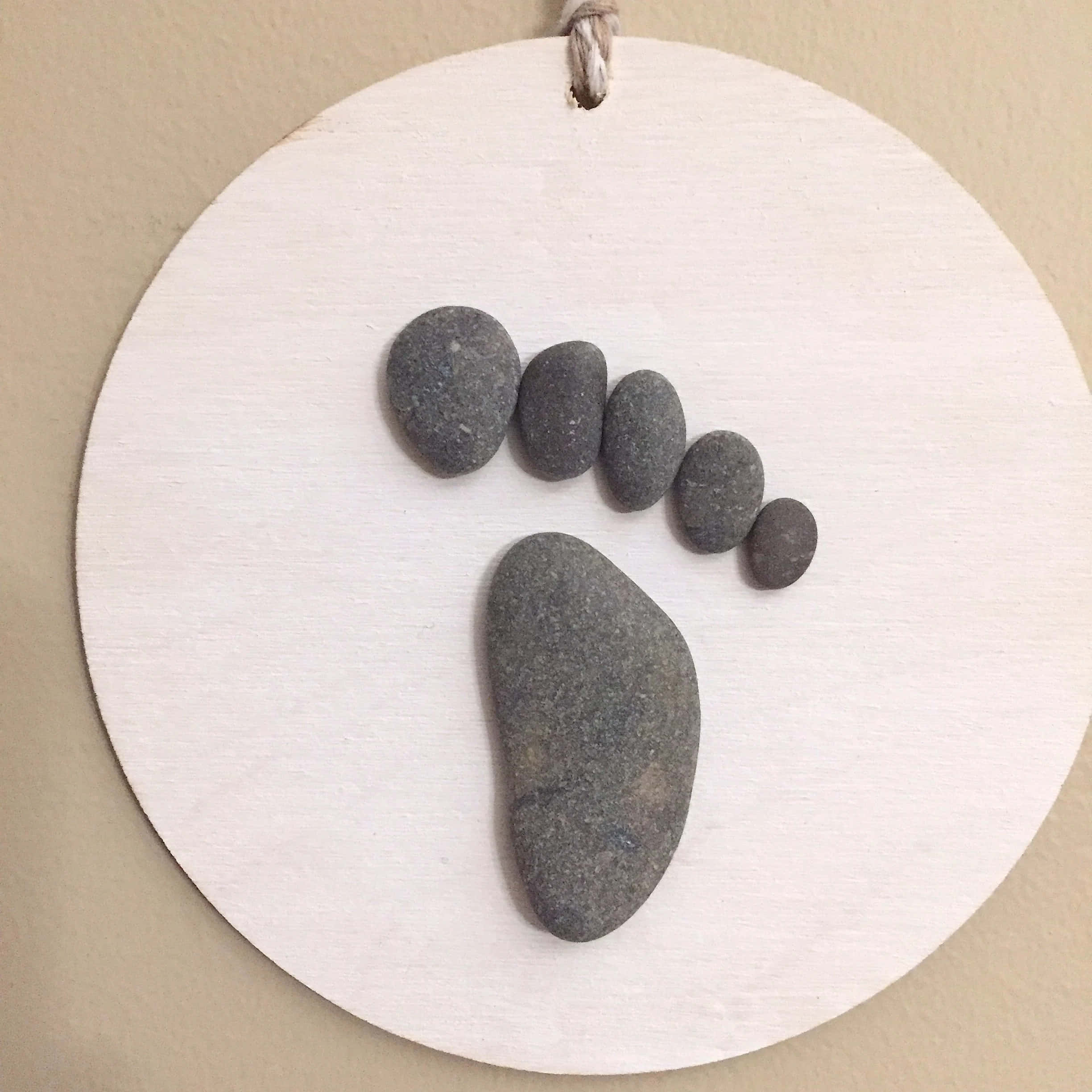 精緻手作 Pebble Art 藝術設計 壁紙 — 一個極簡風格的牆壁掛飾，由光滑的灰色河石排列在圓形白色木盤上形成腳印圖案。