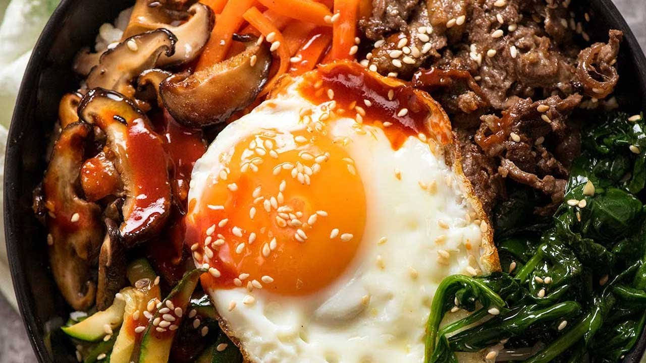 精緻拌飯食材擺盤 壁紙 — 一碗色彩繽紛的韓國石鍋拌飯，上面放著太陽蛋、芝麻和色彩繽紛的炒蔬菜。