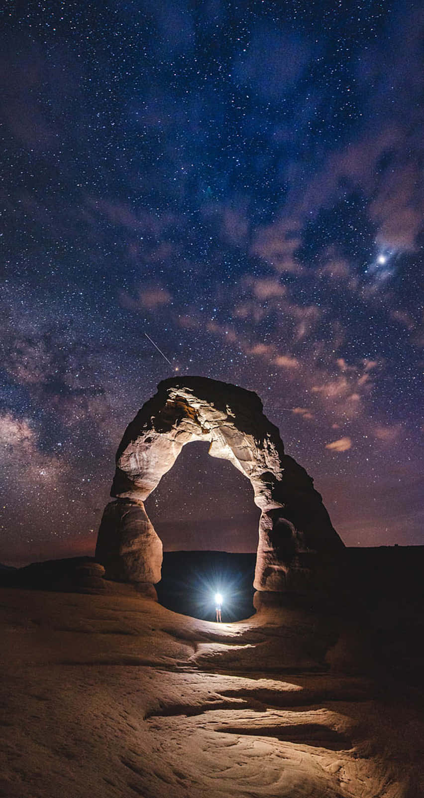 夜晚，一個人在星空下站在天然石拱門下。