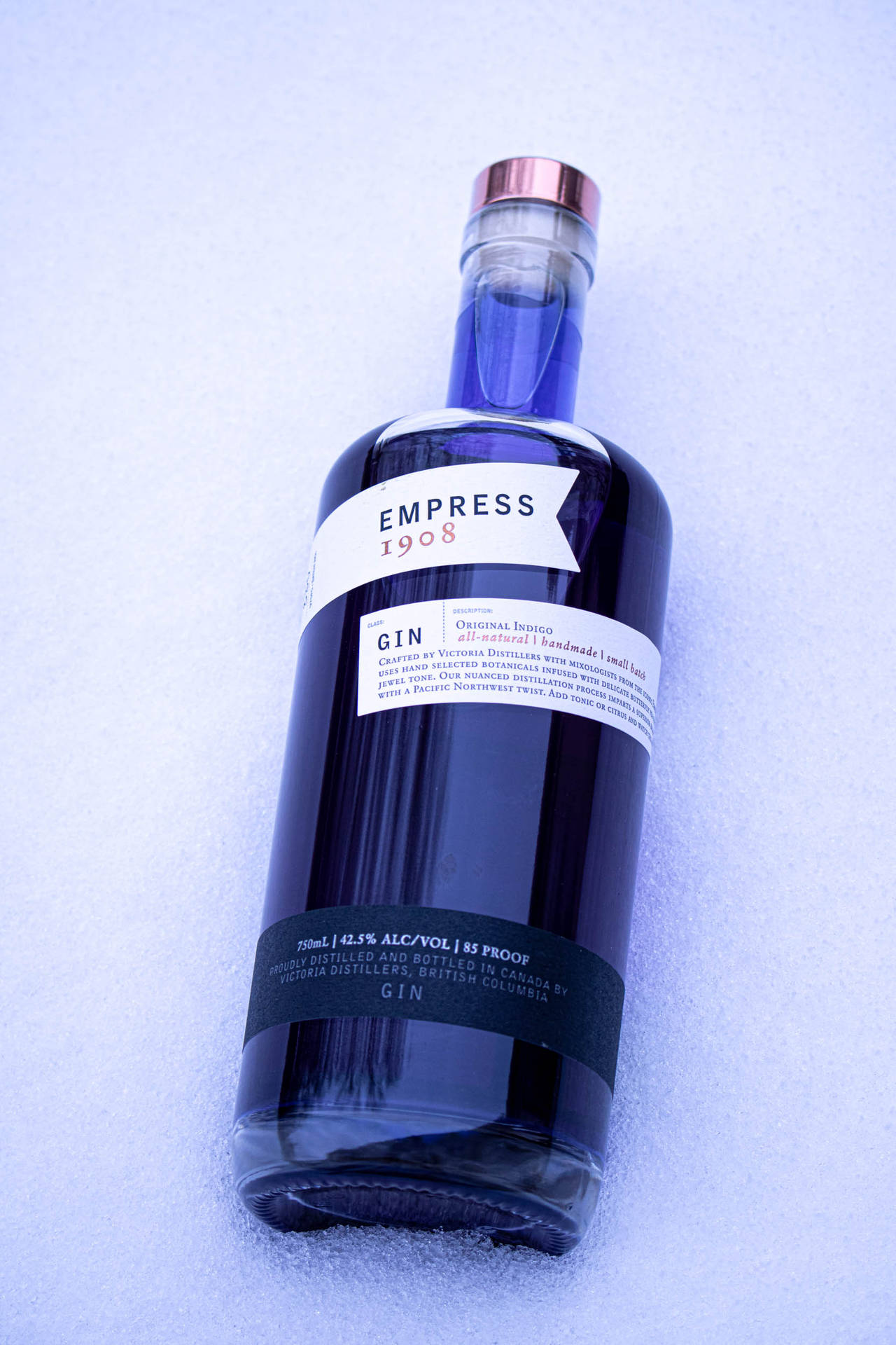 一瓶標有Empress 1908的深藍色氈酒瓶，在藍光下放置在雪地上。