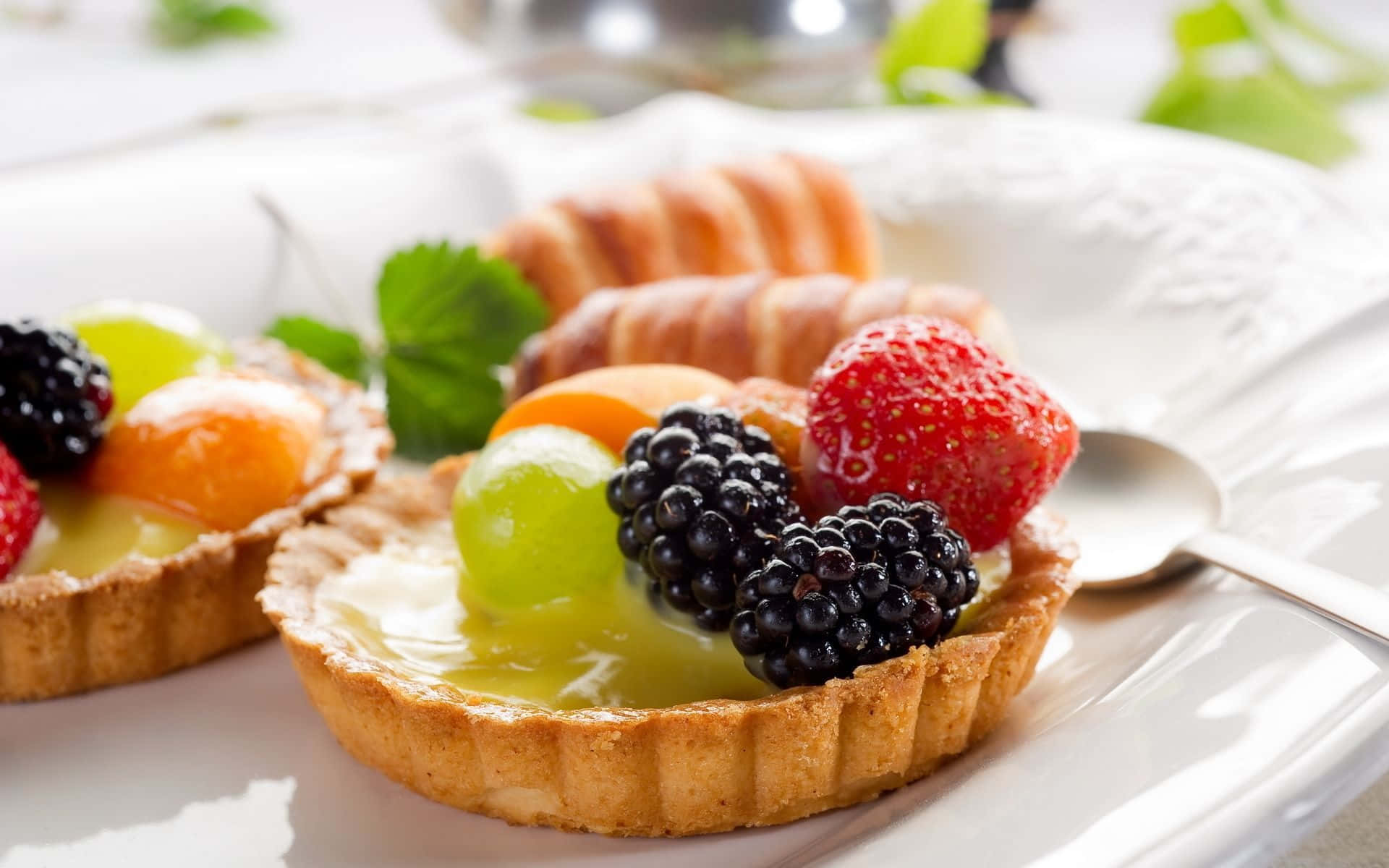Dessert 桌布 壁紙 — 精緻的水果撻，上面鋪滿鮮豔的士多啤梨、黑莓和葡萄，在柔和光線下於白色碟上閃閃發光。