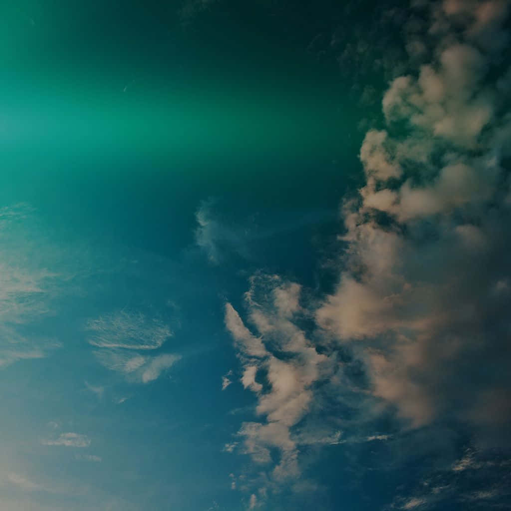 青綠色和藍色的天空，雲朵被綠色極光照亮。