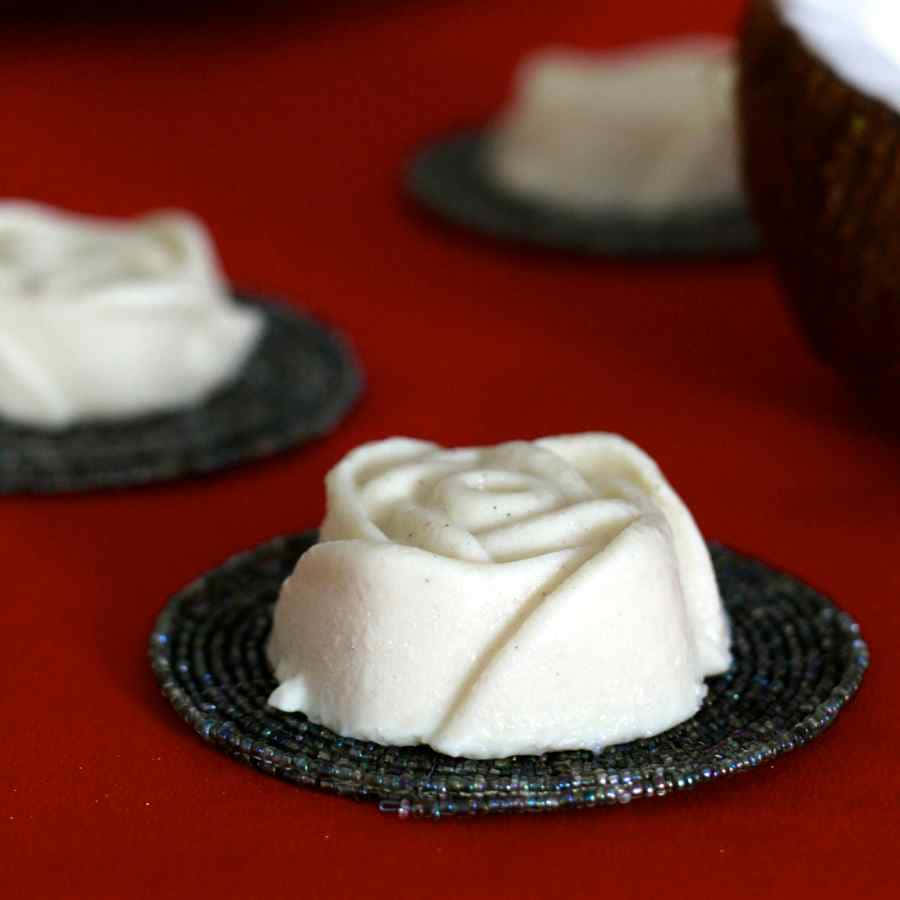 Blancmange 桌布 壁紙 — 精緻的白色玫瑰形狀甜品放在珠飾杯墊上，襯托著濃郁的紅色背景。