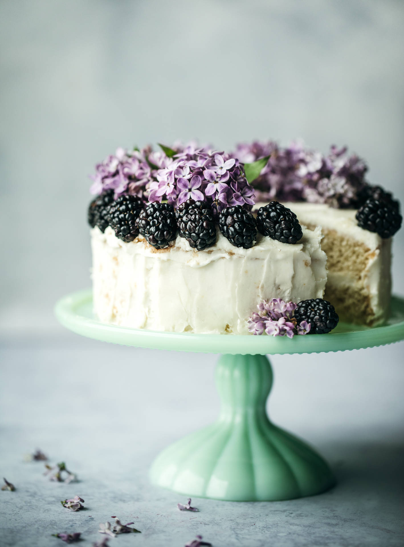 薄荷綠架子上放著一個有黑莓和丁香花的蛋糕。