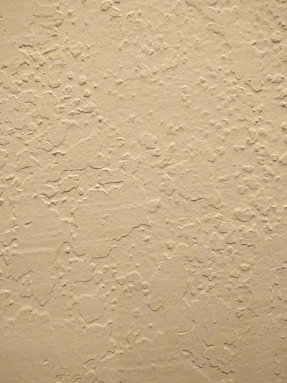 米色紋理牆的特寫，帶有裂縫和凸起。