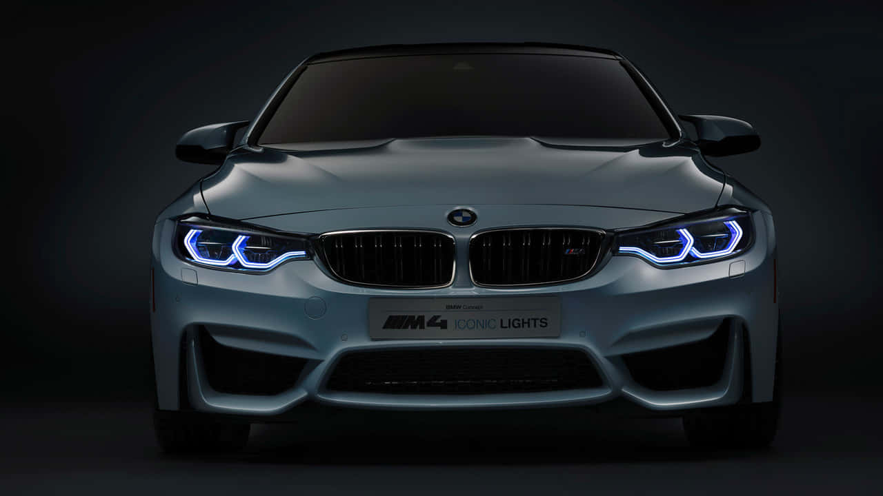 精緻設計的 720p BMW 壁紙 — 時尚的銀色BMW M4跑車在黑暗的攝影棚背景下散發出充滿活力的藍色LED頭燈光芒。