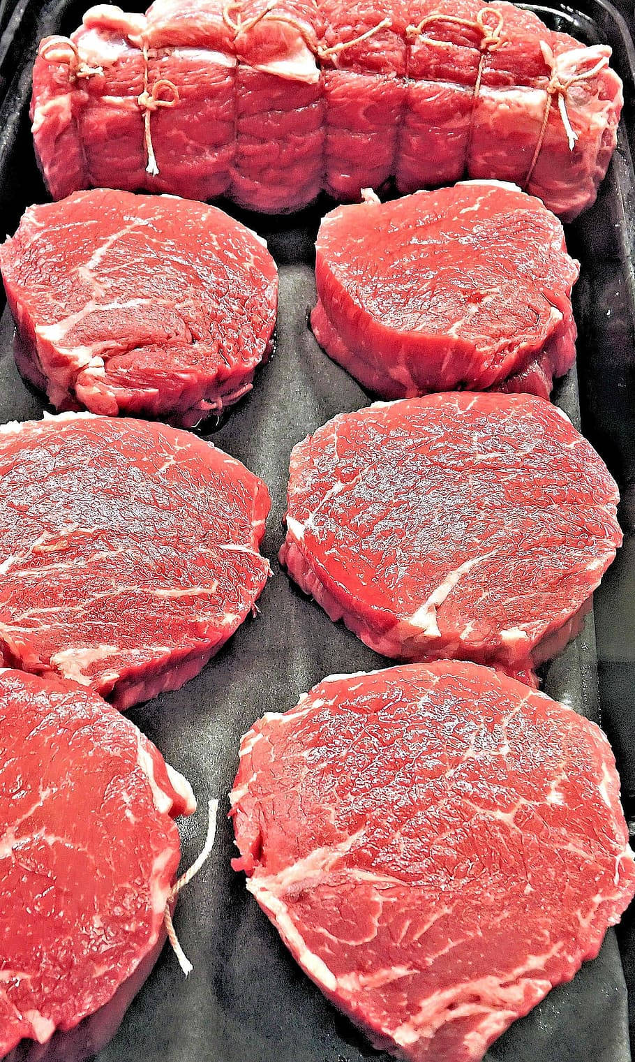 新鮮生牛肉扒和紮好的烤肉放在黑色托盤上。