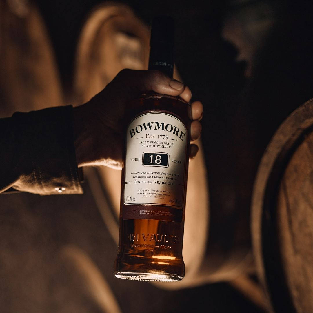 手在桶房裡拿著一瓶 Bowmore 18年威士忌。