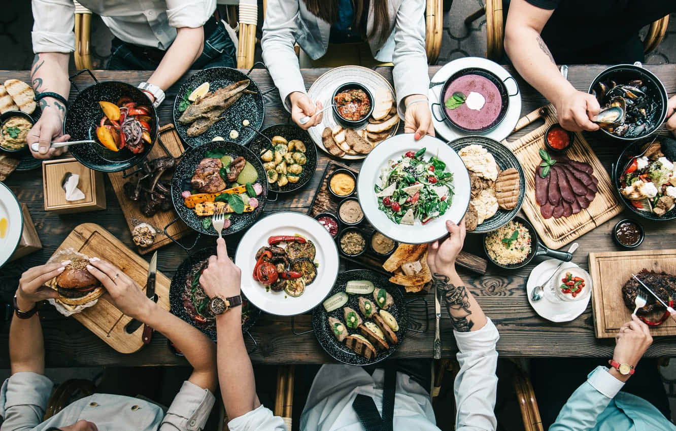 Group of people enjoying a diverse meal together at a wooden table.
