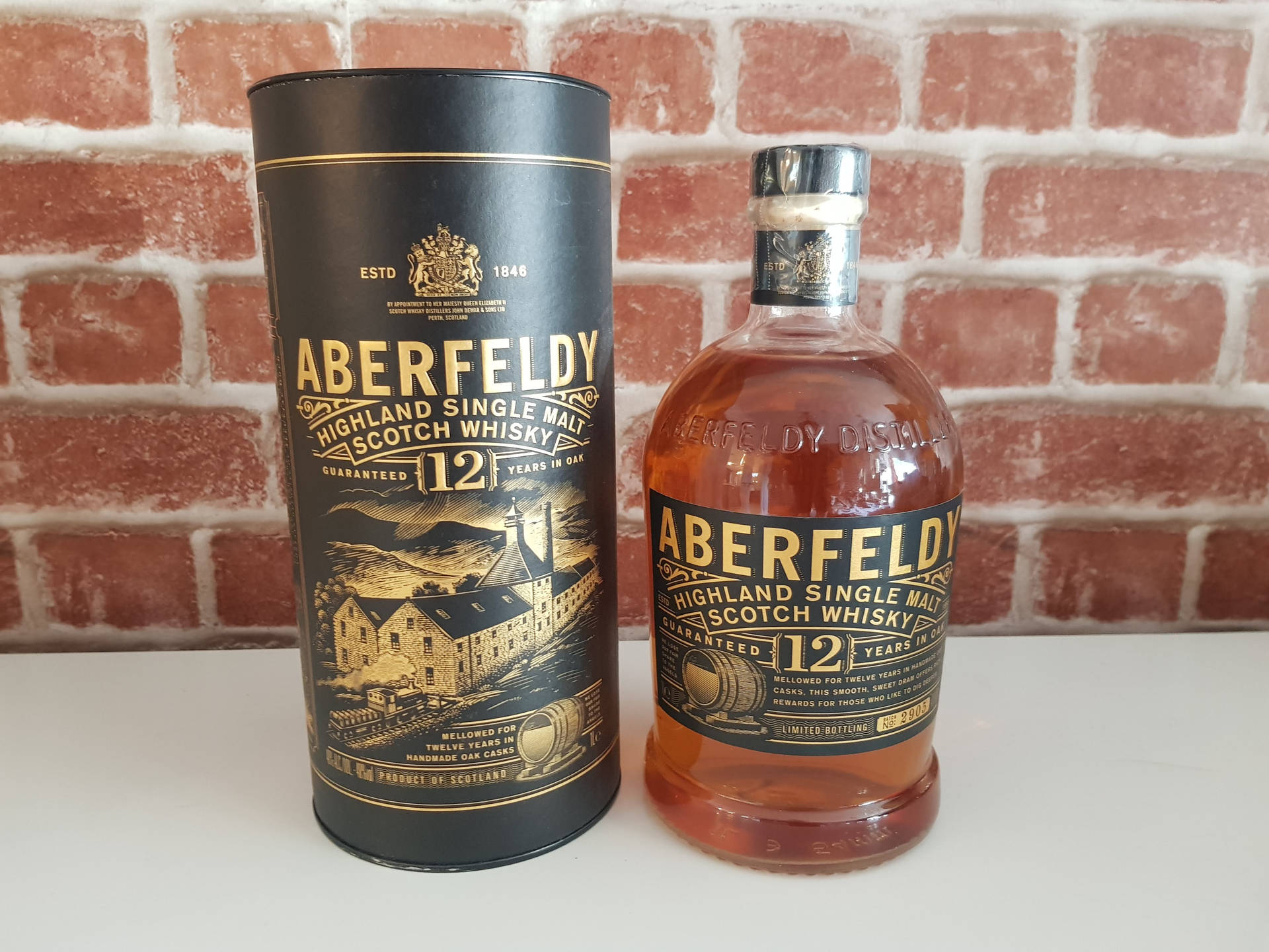 Aberfeldy 12年威士忌酒瓶和禮盒，白色表面配紅磚牆背景。