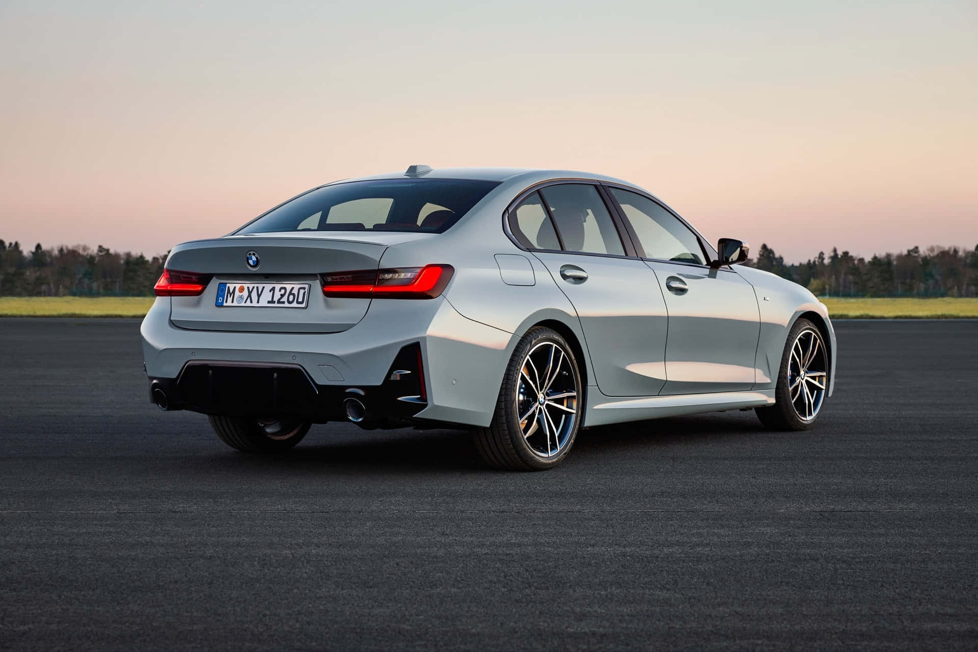 精雕細琢的BMW 壁紙 — 一輛時尚的銀色寶馬3系轎車停在瀝青路上，背景是日落時分柔和的粉紅色和橙色天空。