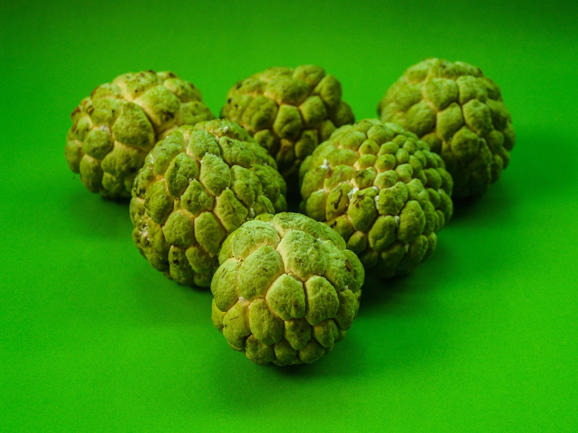 糖蘋果驚豔形狀 壁紙 — 六個綠色嘅牛油果蘋果，表面凹凸不平，排列喺充滿活力嘅純綠色背景上。