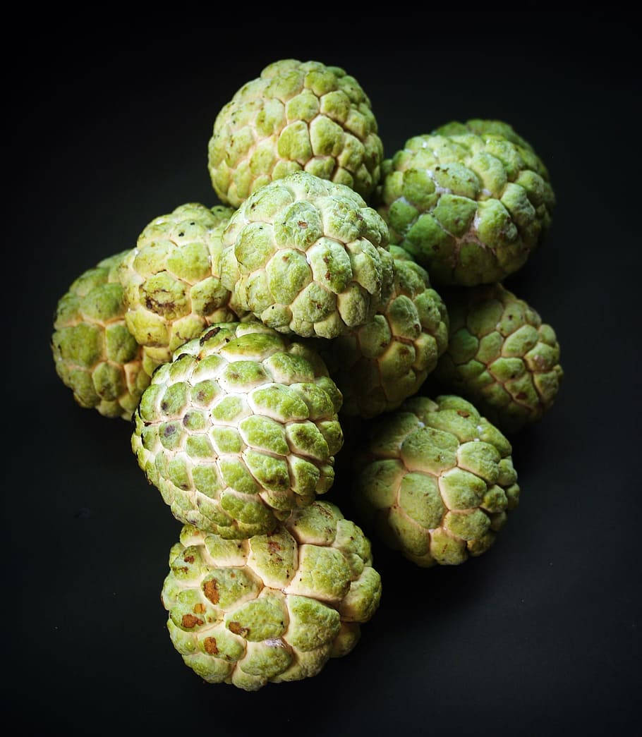 糖蘋果高質攝影 壁紙 — 一堆新鮮的綠色刺果番荔枝，表皮帶有紋理，放在純黑色背景上。