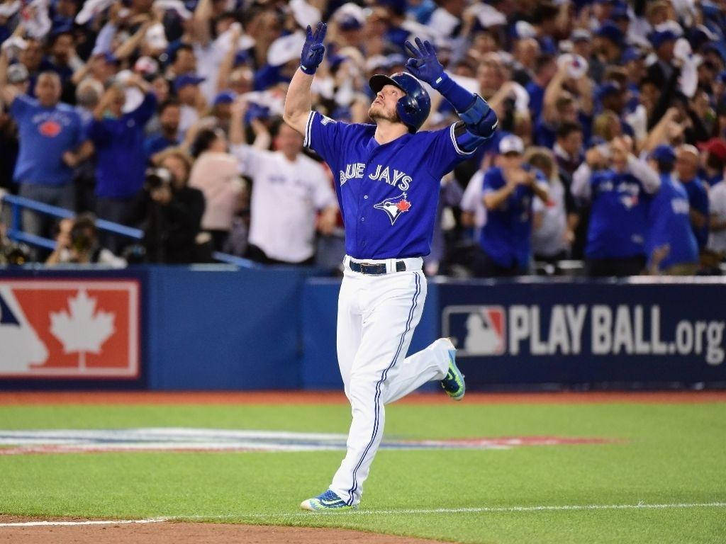 身穿藍鳥隊球衣的棒球選手在球場上高舉雙臂慶祝。