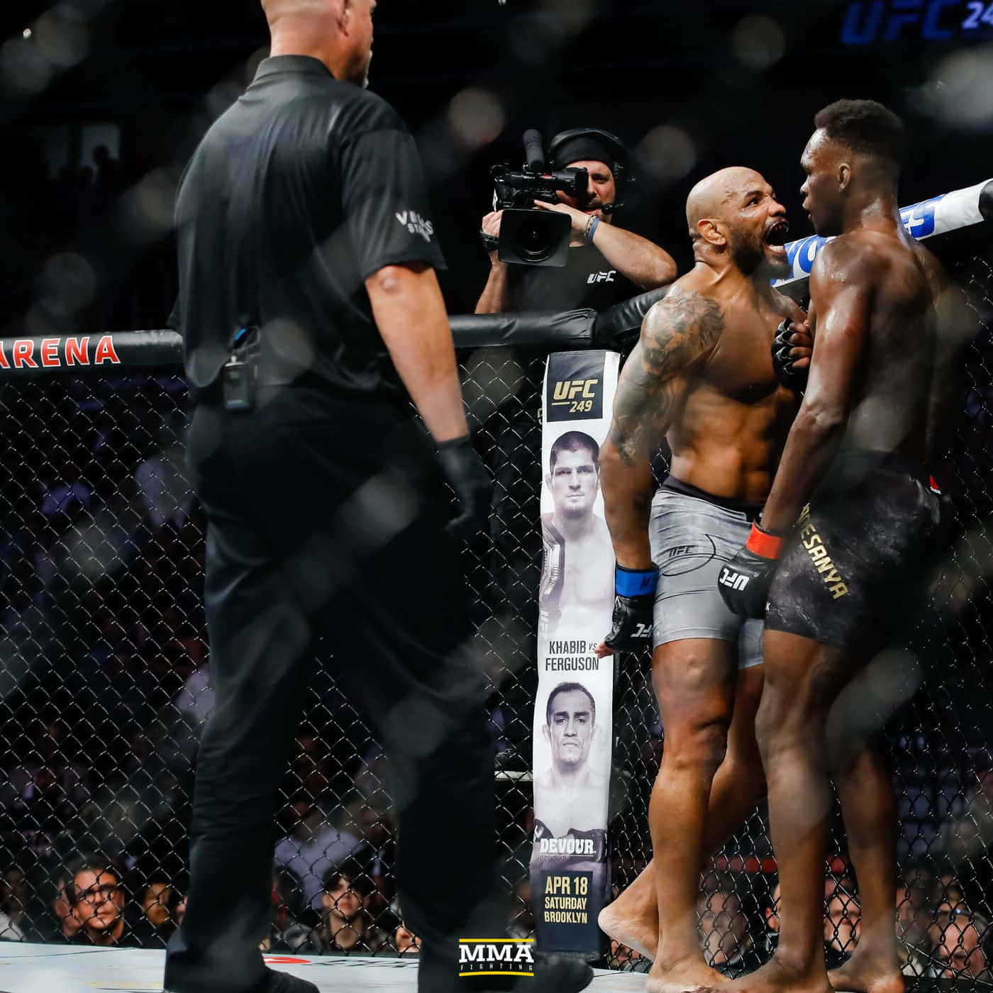 約爾·羅梅羅對決以色列·阿德薩尼亞 UFC 248 壁紙 — 兩位肌肉發達的MMA拳手在明亮的場館燈光下於鐵籠中對峙，附近有裁判和攝製組。
