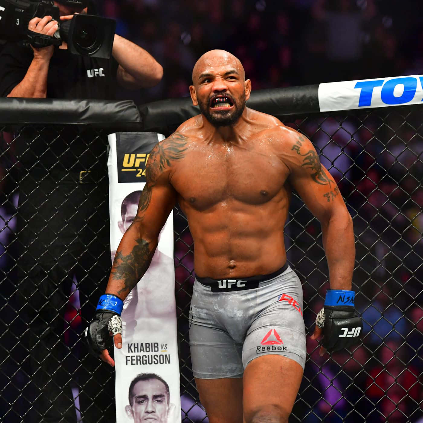 約爾·羅梅羅於UFC 248賽事敗北反應 壁紙 — 一位肌肉發達的UFC拳手在八角籠內勝利咆哮，紋身和汗水在場館燈光下閃閃發光。