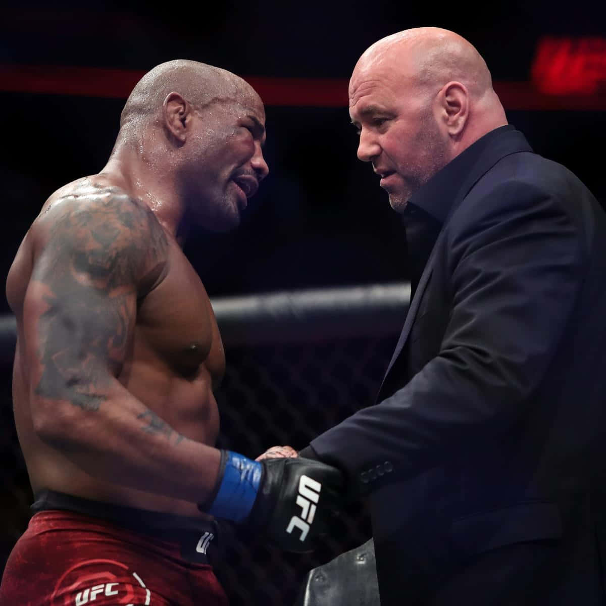 約爾·羅梅羅與UFC主席達納·懷特 壁紙 — 一名肌肉發達、有紋身的拳手穿著紅色短褲，在UFC八角籠內與一名身穿黑色西裝的光頭男子握手。