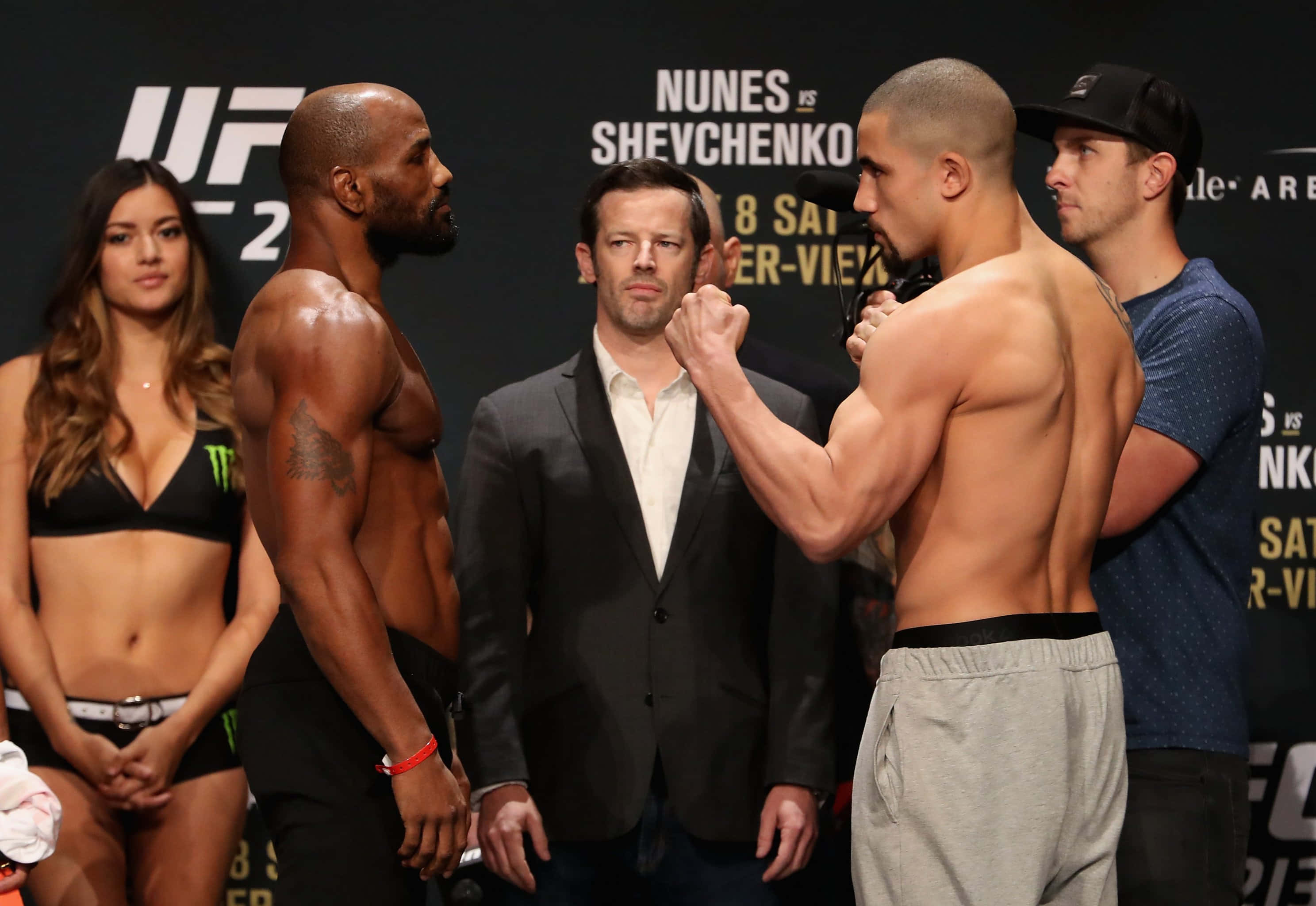 約爾·羅梅羅與羅伯特·惠特克於UFC 213稱重儀式 壁紙 — 兩位肌肉發達的UFC拳手在明亮的場館燈光下，以高度專注和舉起的拳頭在稱重儀式上對峙。