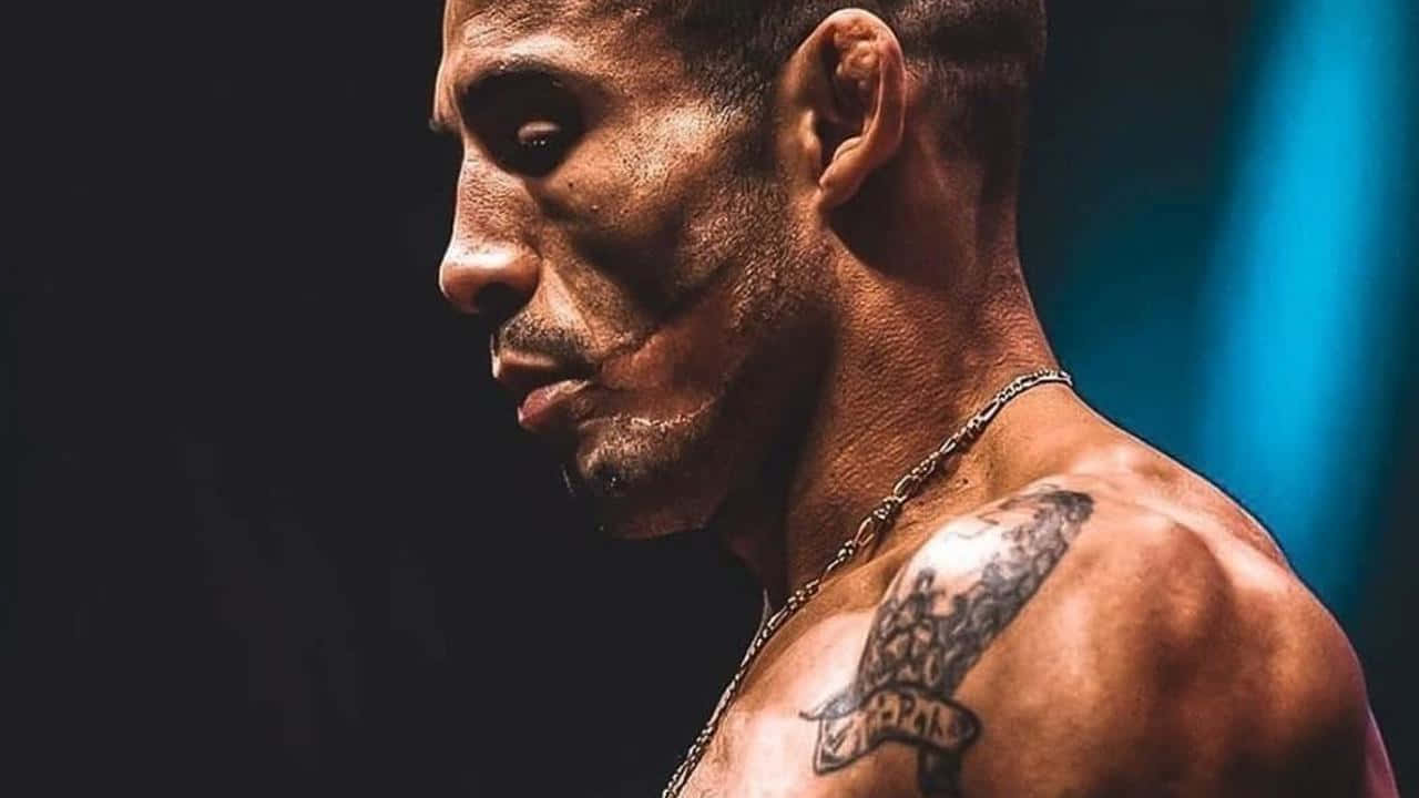 一個汗流浹背、肩膀有紋身、戴著鏈條項鍊的肌肉發達男人，凝視著。