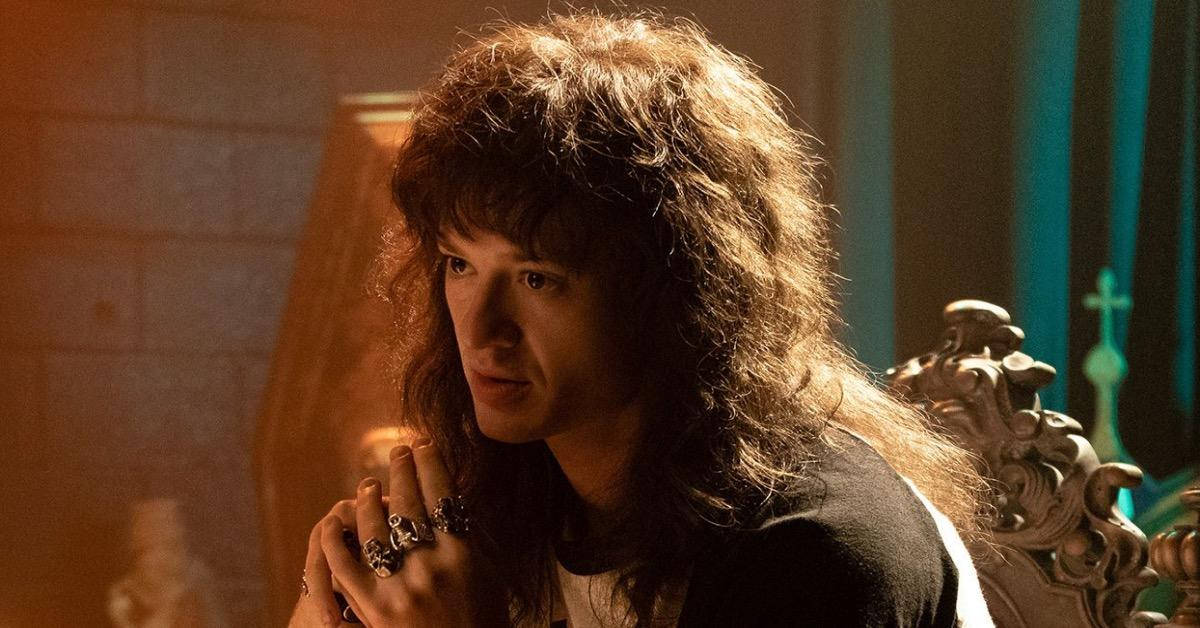 約瑟夫·奎恩《怪奇物語》劇照 壁紙 — 一名擁有豐盈捲髮的男子坐在華麗的椅子上，沐浴在溫暖的金色光線中，背景是石牆和藍綠色窗簾。