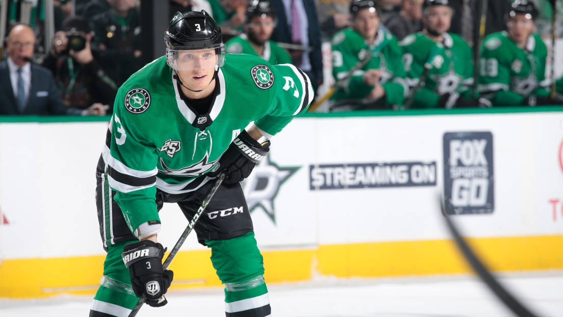 約翰·克林格伯格 NHL 球員海報照 壁紙 — 一名達拉斯星隊的冰球運動員穿著綠色球衣，在比賽中激烈地蹲在冰上，背景有隊友和攝影師。