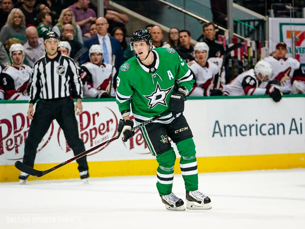 約翰·克林格伯格NHL合適海報照片 壁紙 — 達拉斯星隊的綠色球衣冰球運動員在冰上激烈滑行，背景有裁判和人群。