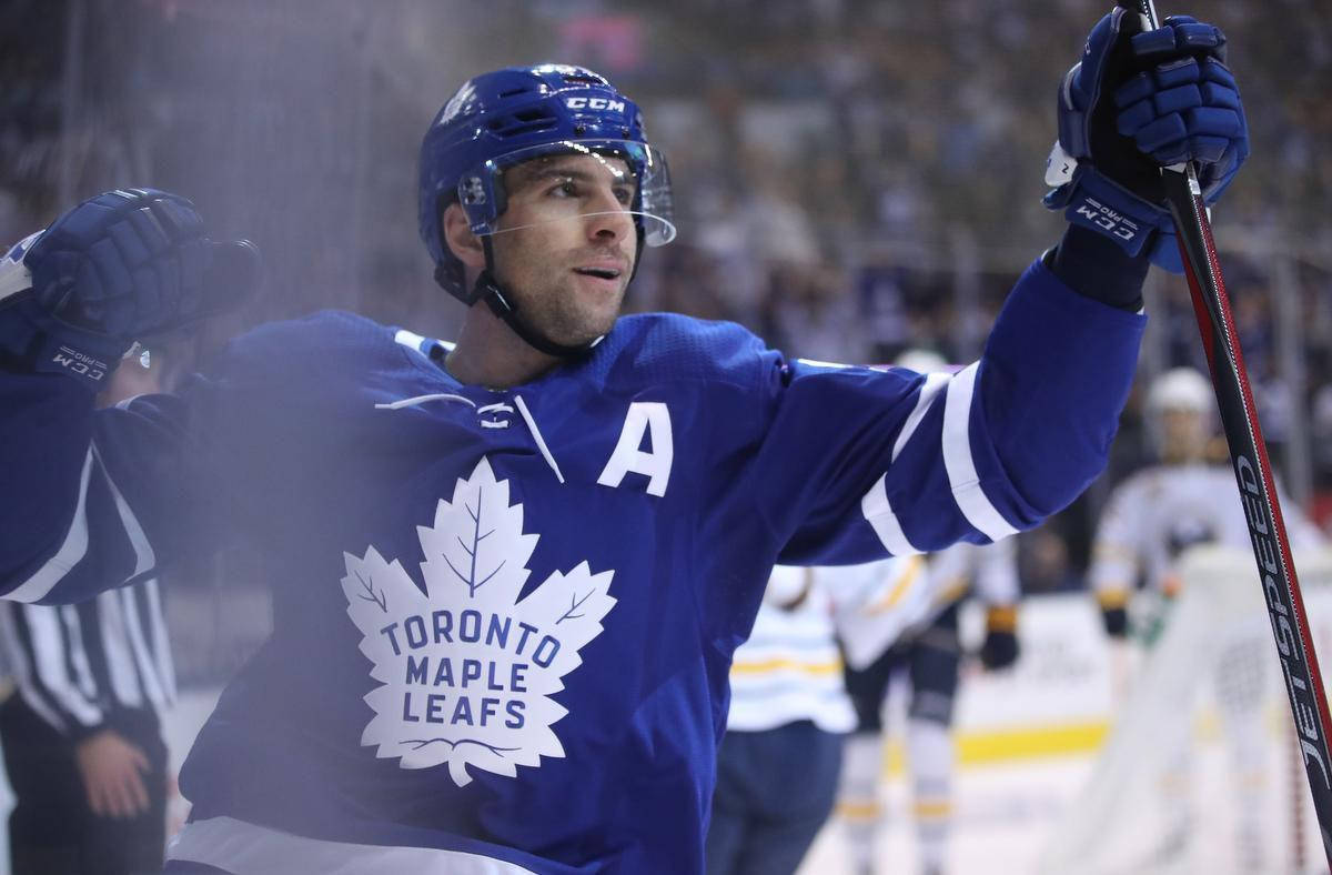 約翰·塔瓦雷斯多倫多楓葉隊NHL慶祝海報 壁紙 — 一名身穿藍色球衣的多倫多楓葉隊冰球球員在冰上高舉球棍和手套慶祝。