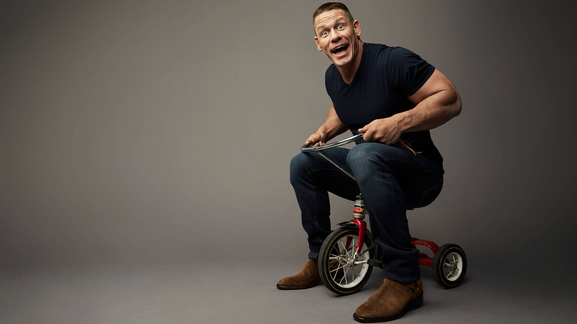 John Cena 喺工作室入面踩紅色三輪車時微笑。