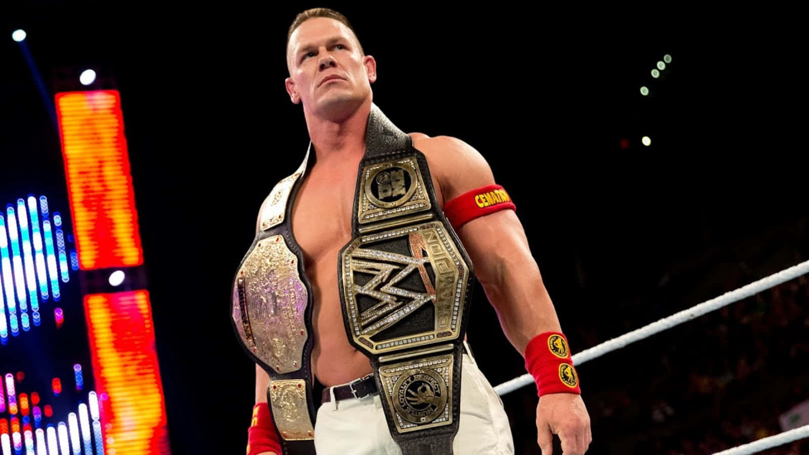 John Cena 桌布 壁紙 — 約翰·辛納在明亮的競技場燈光下，腰間掛著多條冠軍腰帶，在摔角擂台上勝利地站著。