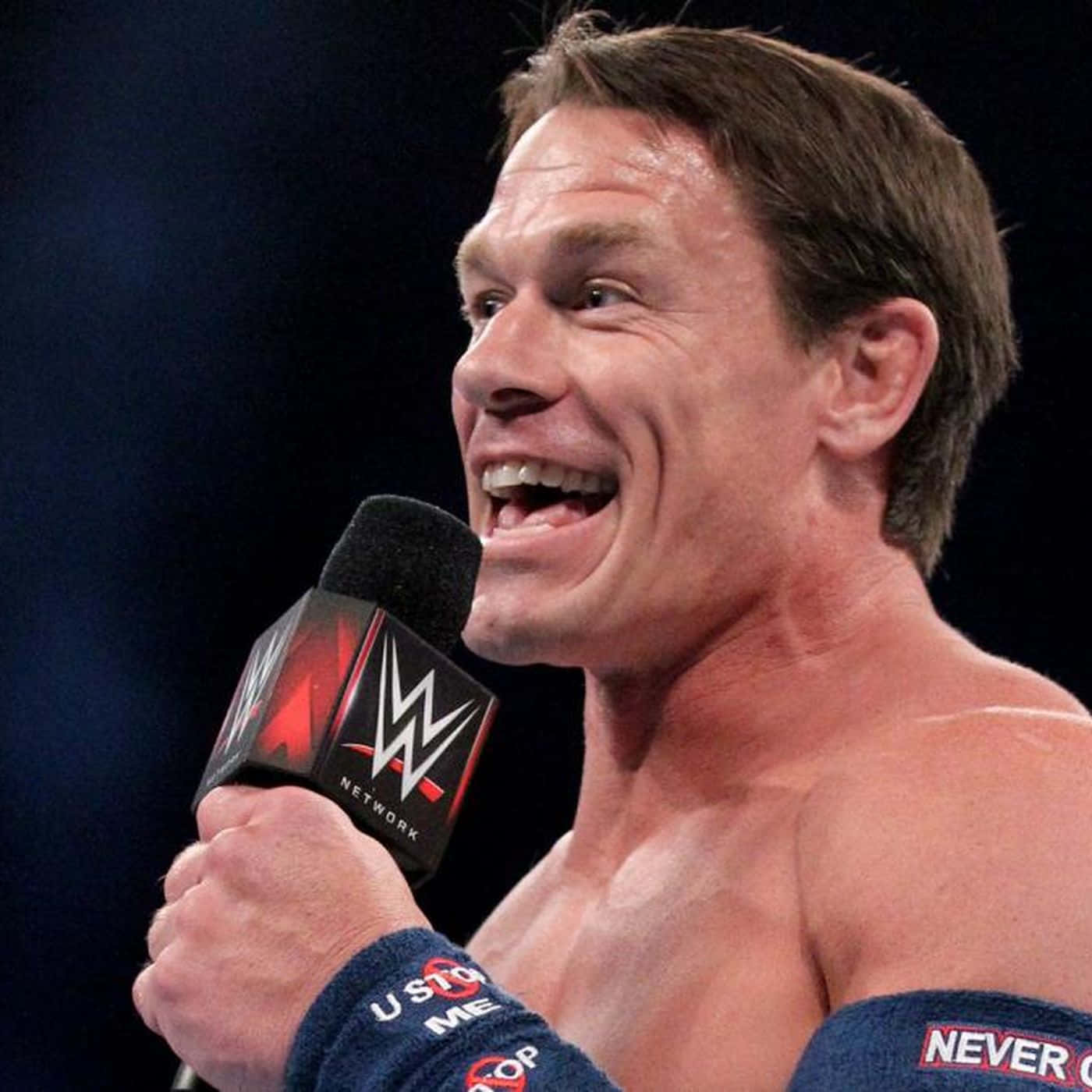 John Cena 桌布 壁紙 — 約翰·辛納在明亮的舞台燈光下，於現場活動中手持WWE Network麥克風，咧嘴大笑。