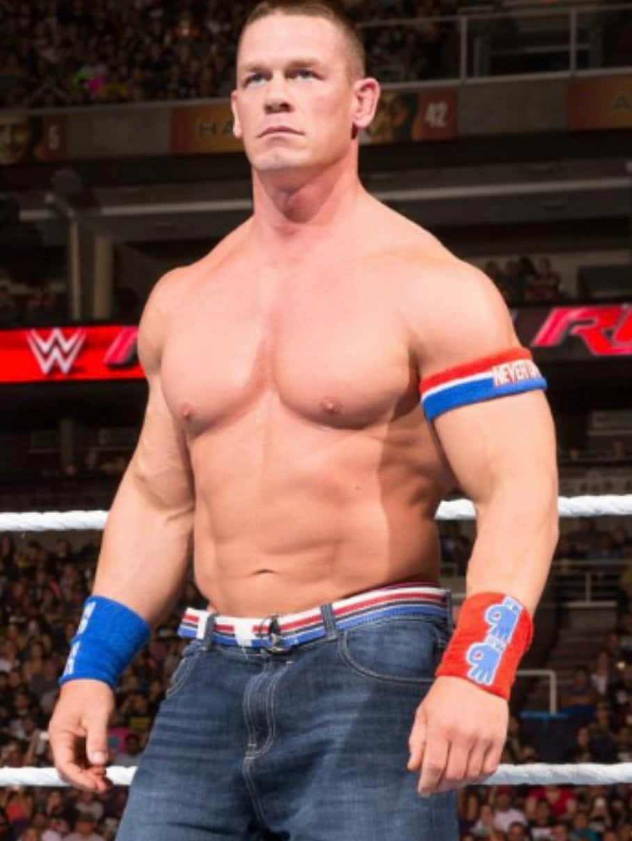 John Cena 桌布 壁紙 — 約翰·辛納赤裸上身站在摔角擂台上，穿著藍色牛仔褲和愛國腕帶，表情專注。