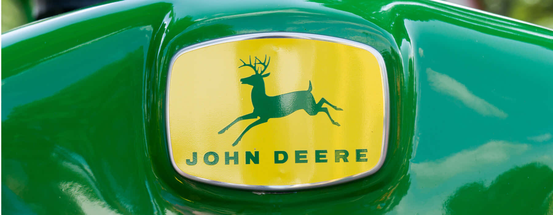 John Deere 桌布 壁紙 — 約翰迪爾標誌特寫，黃色背景上有一隻跳躍的鹿，背景是光澤的綠色機械。