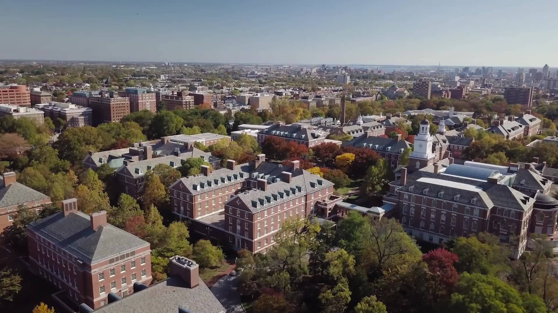 藍天下，磚造建築與秋樹交織的大學校園鳥瞰圖。