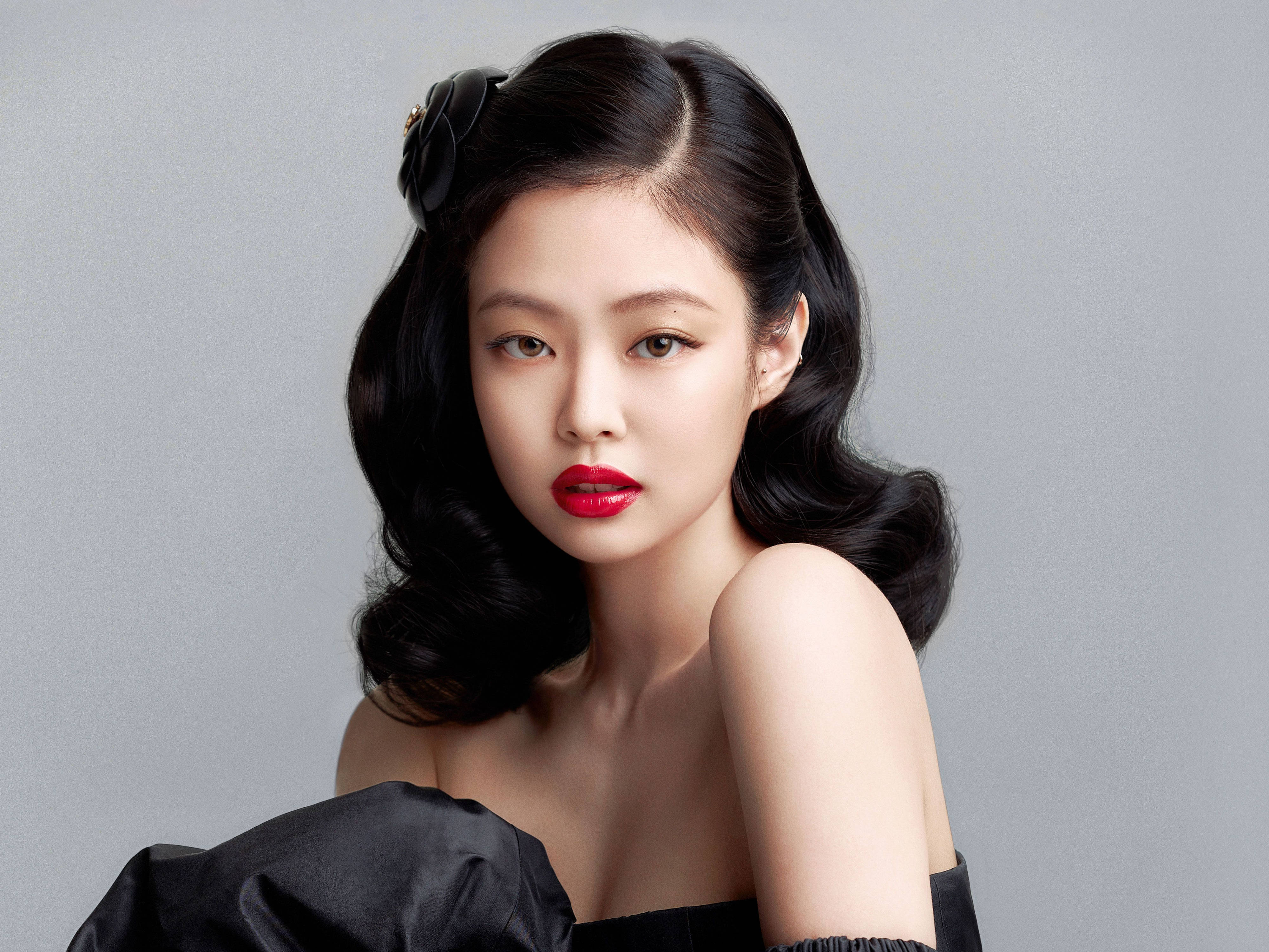 紅唇 Jennie Kim 黑色造型桌面壁紙 壁紙 — 一位擁有光澤黑色波浪髮型和鮮豔紅唇的女性，直視著柔和的灰色背景。