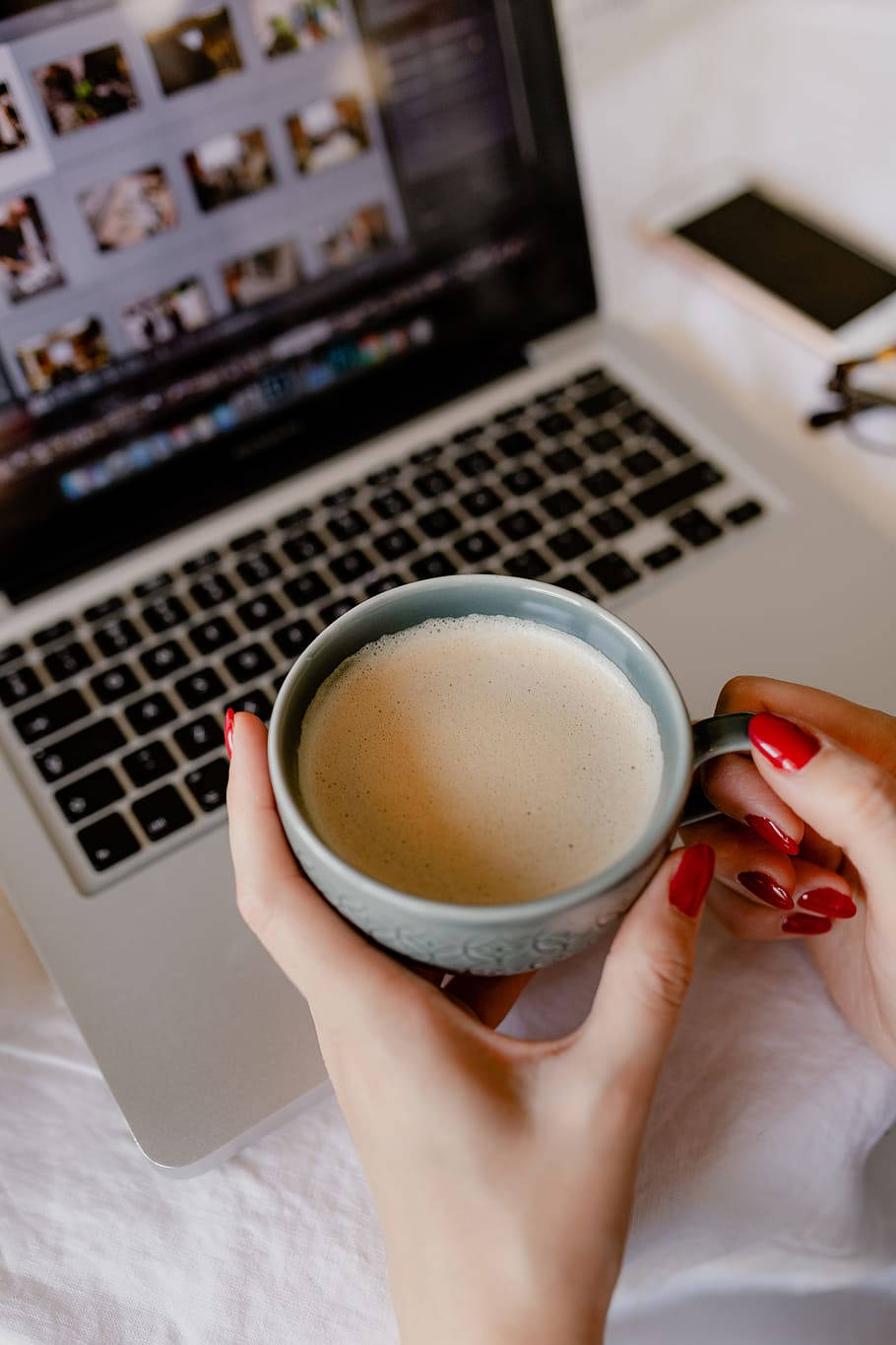 Best Laptop 桌布 壁紙 — 紅指甲的手在打開的筆記本電腦旁捧著冒煙的杯子，筆記本電腦顯示照片縮略圖。