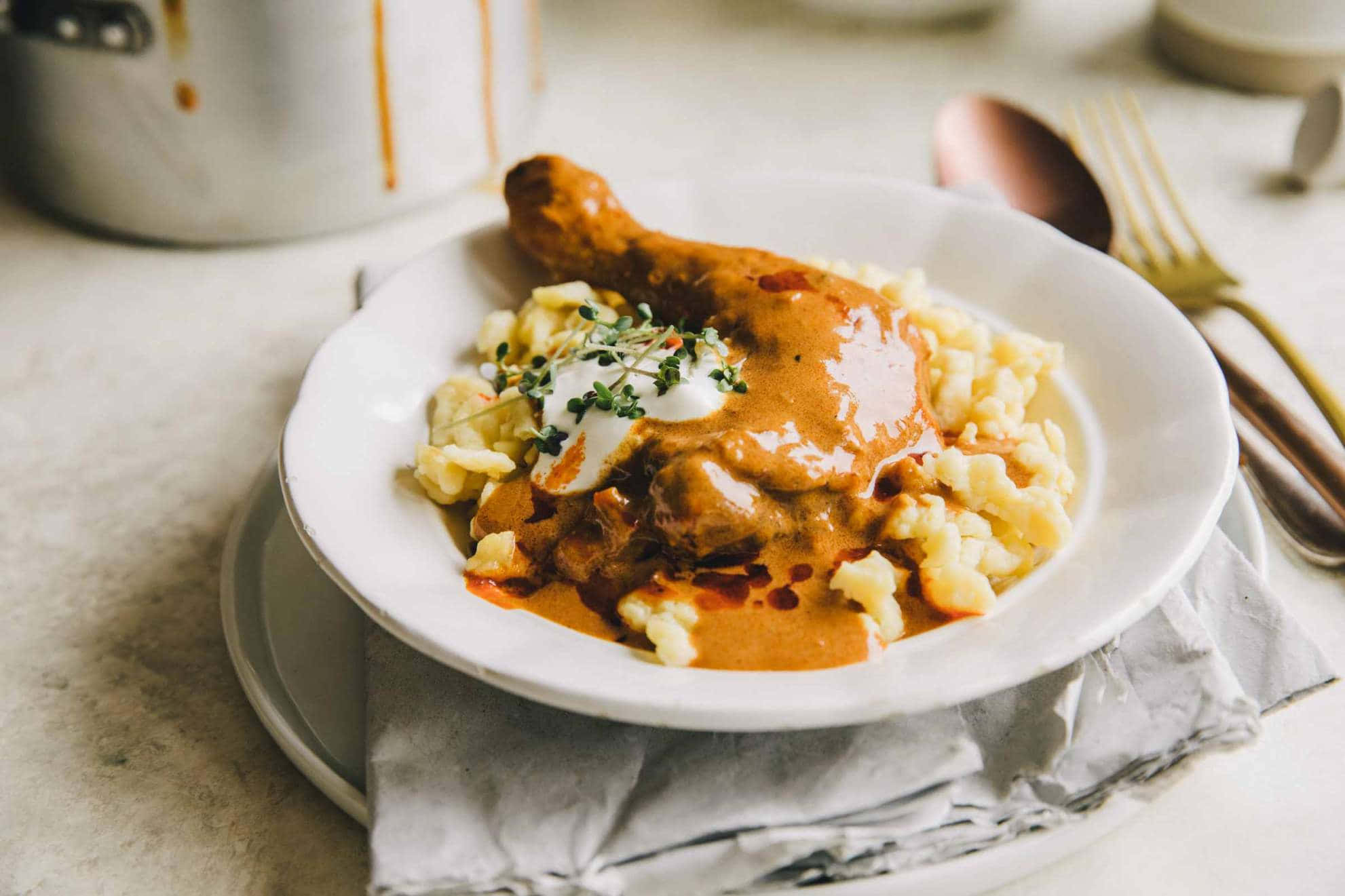 紅椒燉雞腿配 Spaetzle 麵 壁紙 — 白碟上，奶油雞腿配濃郁醬汁，置於鬆軟薯蓉上，以新鮮香草裝飾。