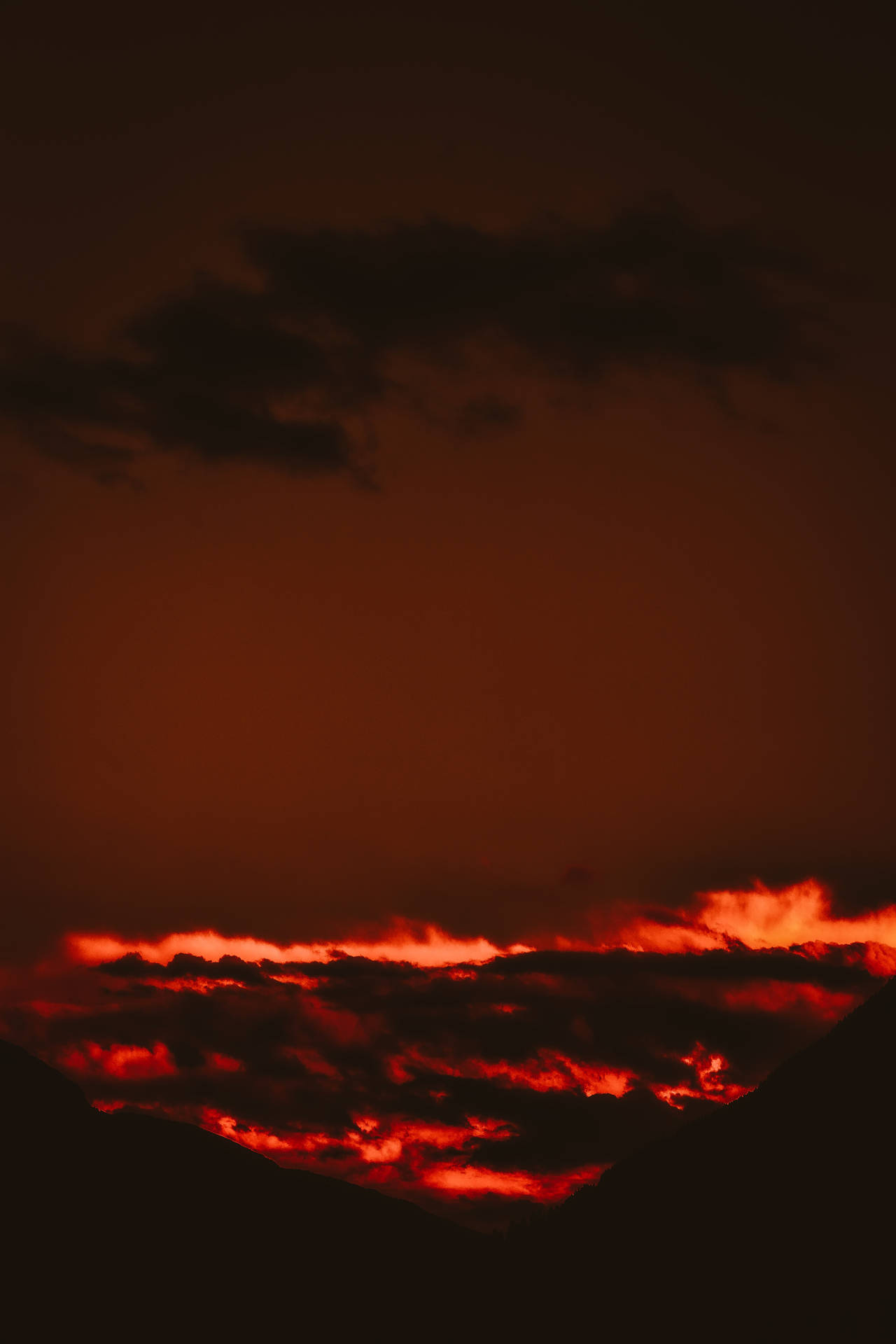 黑暗山巒輪廓上方的火紅日落雲彩