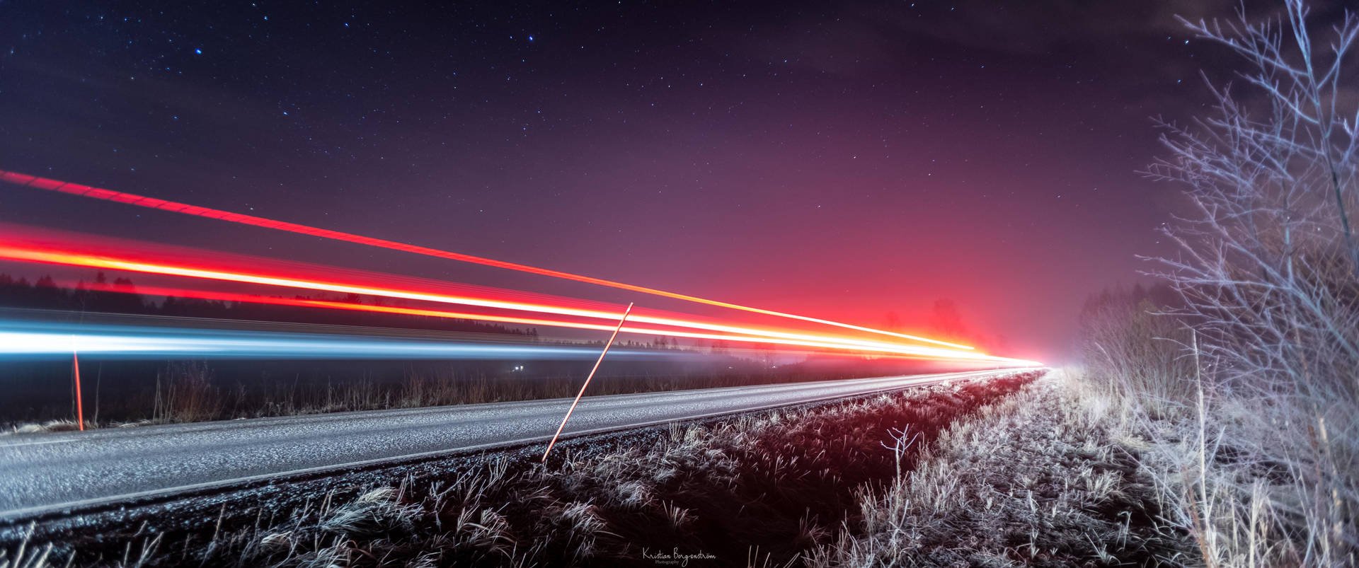 夜晚結冰的路邊，星空下汽車燈光形成的光條。