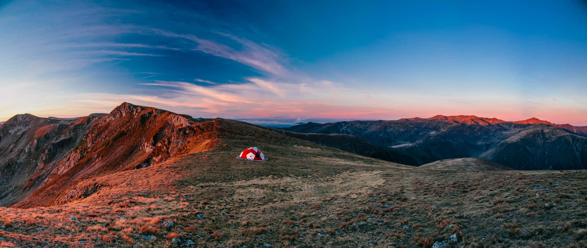 日落時分，在層層疊疊的山峰和漸變天空下的山脊上搭建的紅白帳篷。