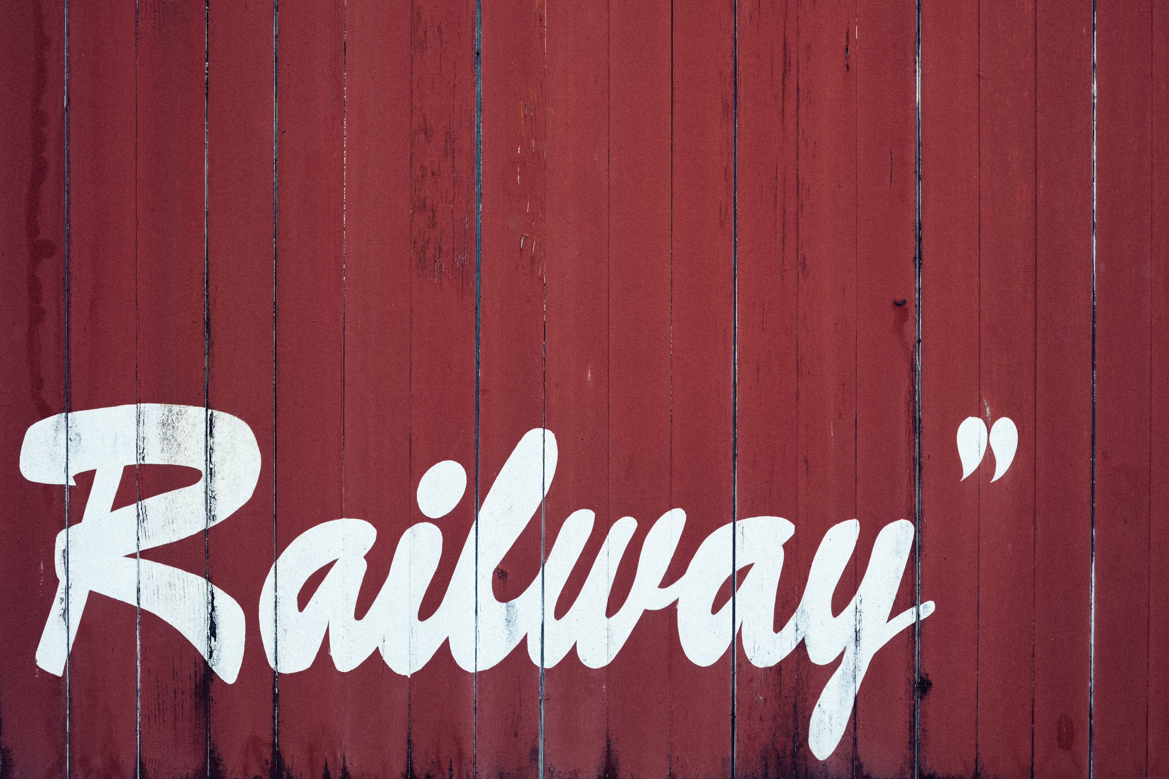 紅白鐵路 壁紙 — 粗體白色草書 'Railway' 文字繪製在風化的紅色木板上，木紋清晰可見，油漆剝落。