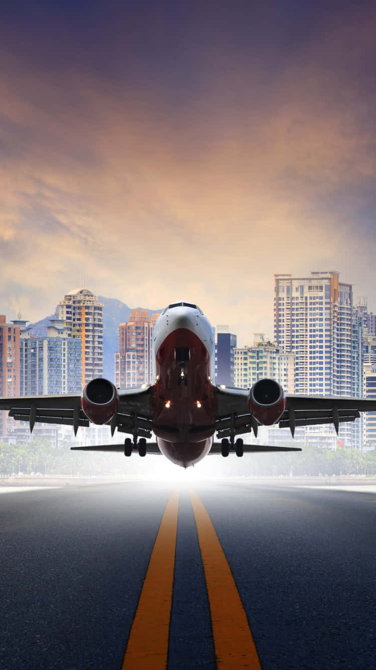 紅白飛機起飛安卓飛機壁紙 壁紙 — 一架商用飛機在日落時從跑道起飛，背景是現代城市天際線和山脈。