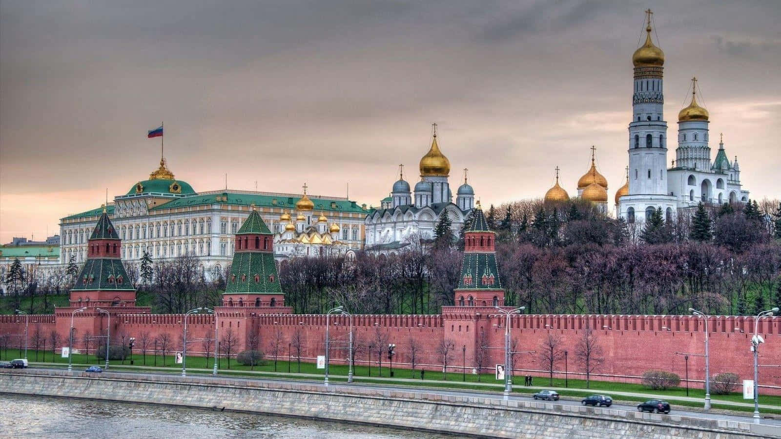 Russia 桌布 壁紙 — 紅磚克里姆林宮城牆和金色圓頂大教堂在暮色中聳立於河畔，天空陰沉灰暗。
