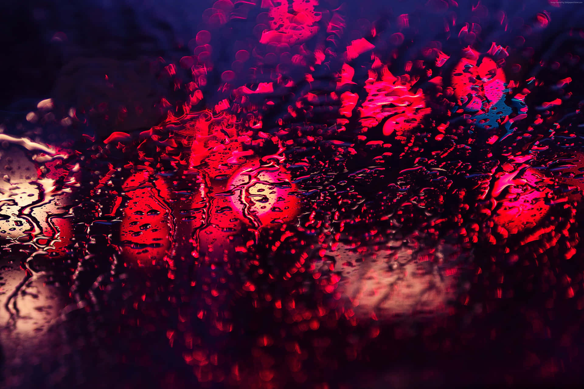 紅紫背景上的雨滴窗景 壁紙 — 鮮豔的紅色和藍色燈光透過被雨淋濕的玻璃變得模糊，營造出憂鬱的城市夜景。