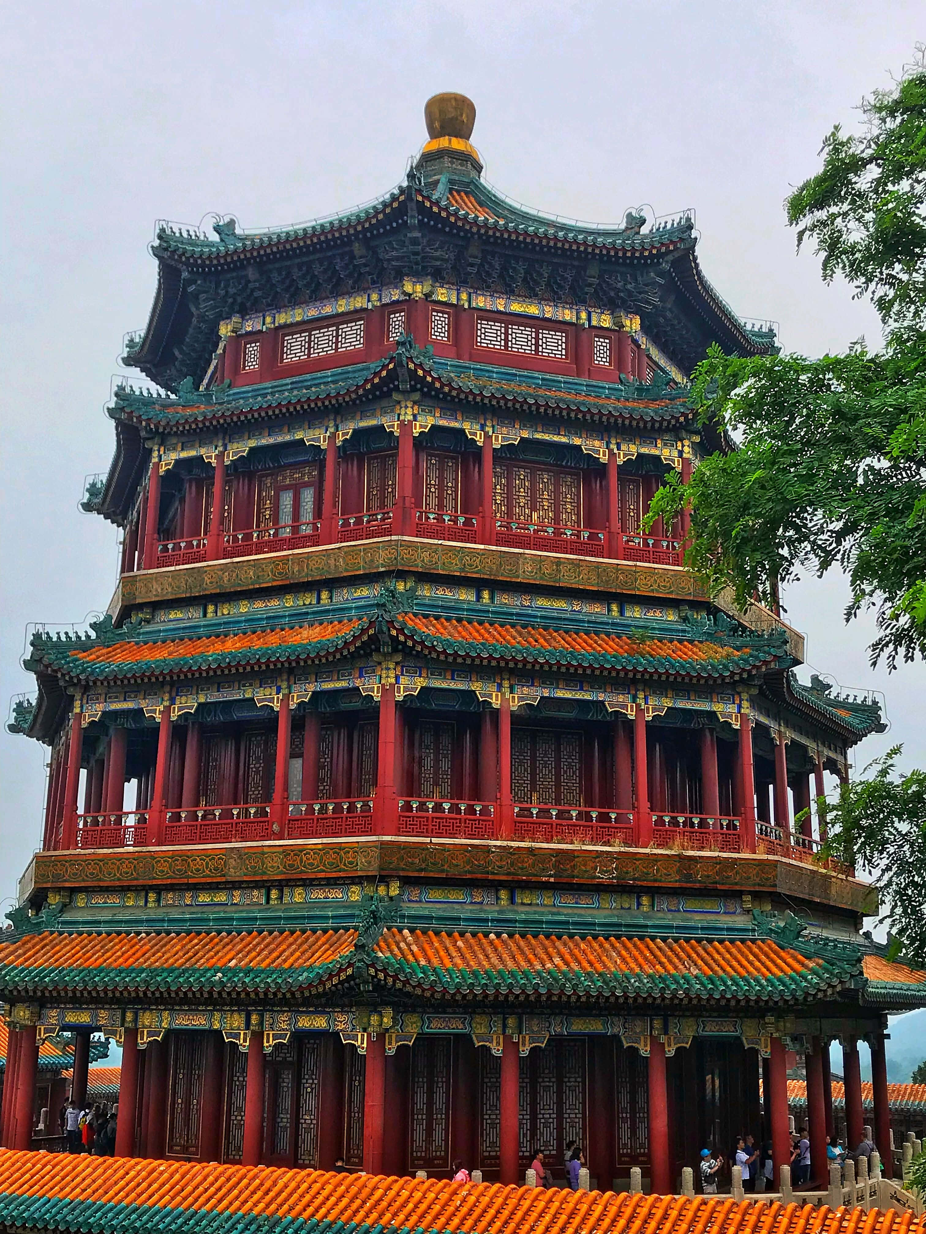 紅綠相間的圓明園 壁紙 — 一座宏偉的多層中式寶塔，紅色柱子、綠色屋頂，在陰天中高聳，周圍環繞著茂密的綠樹。